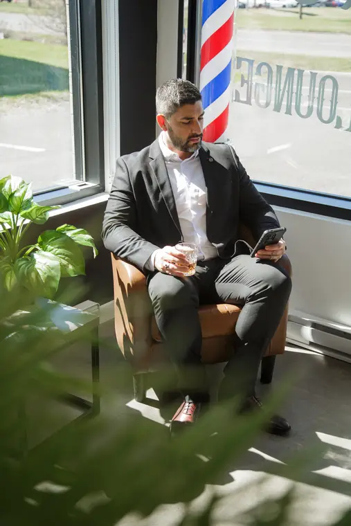 Homme en complet assis dans un salon, verre à la main