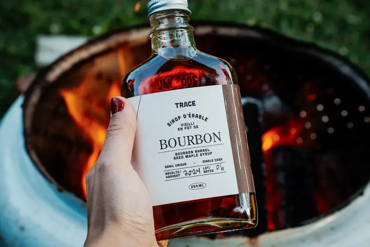 Bouteille de sirop d’érable vieilli au bourbon devant un feu